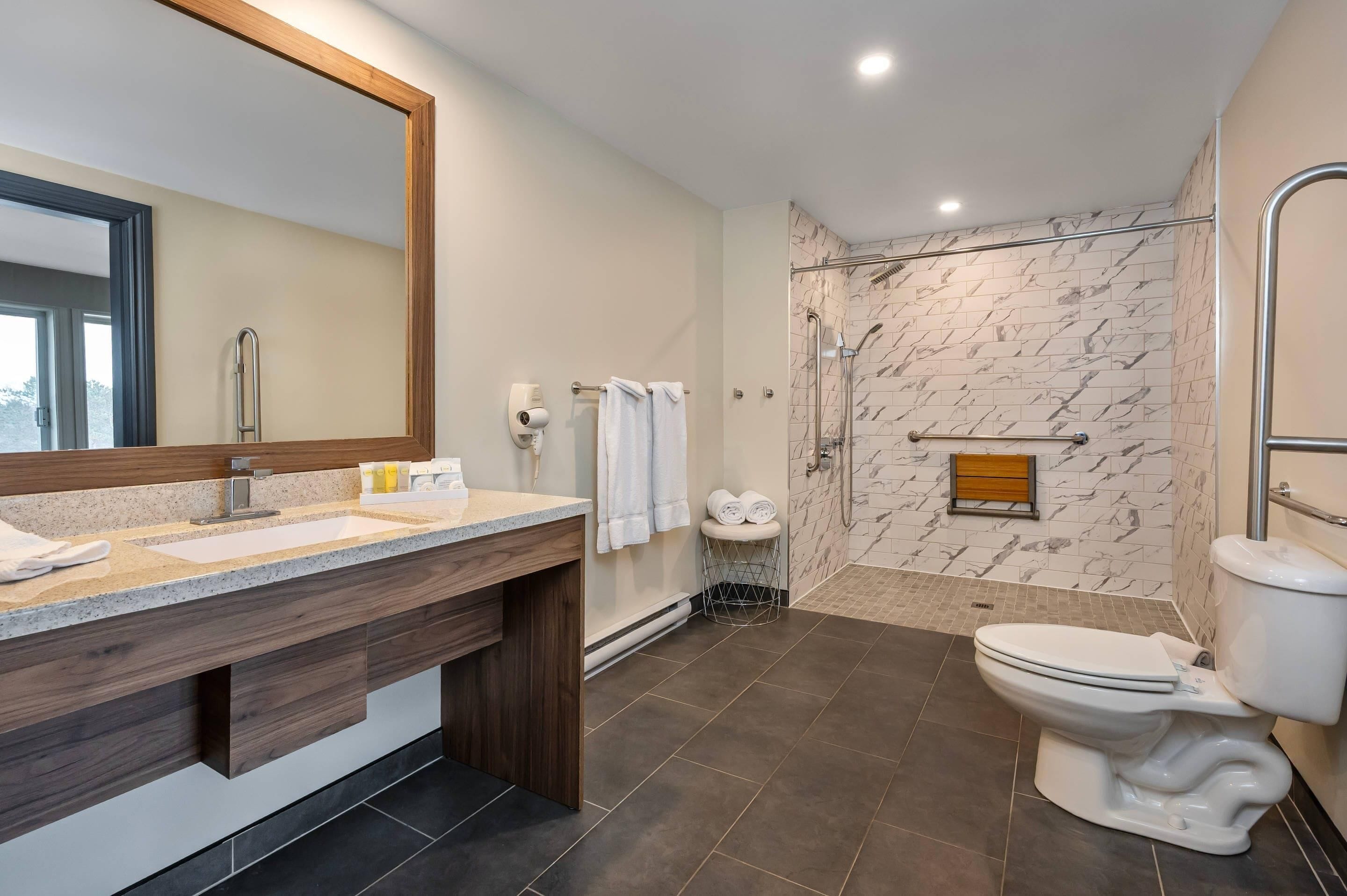 Une salle de bain moderne avec un grand miroir, deux vasques, une douche avec une porte en verre et des toilettes.