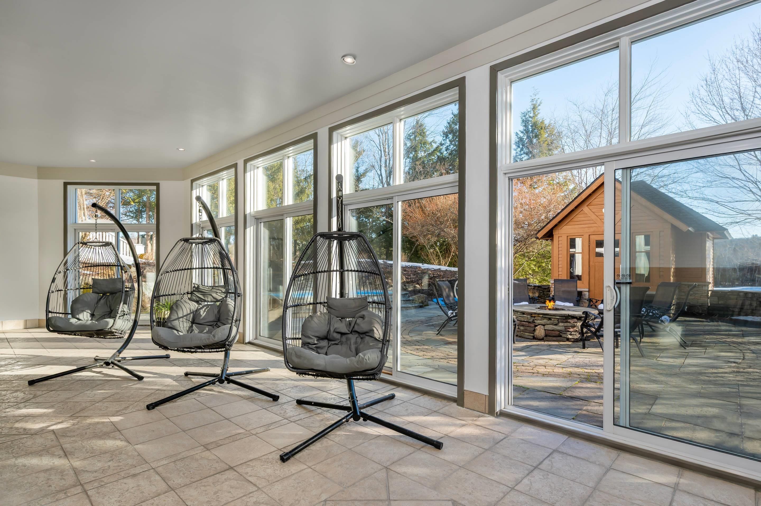 A spacious room with large windows, a stone fireplace, and two hanging chairs.