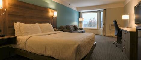 A hotel room with a large bed, a desk, a chair, a television, and a window with a view of trees.