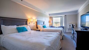 A hotel room with two beds, a desk, a television, and a window with a view.