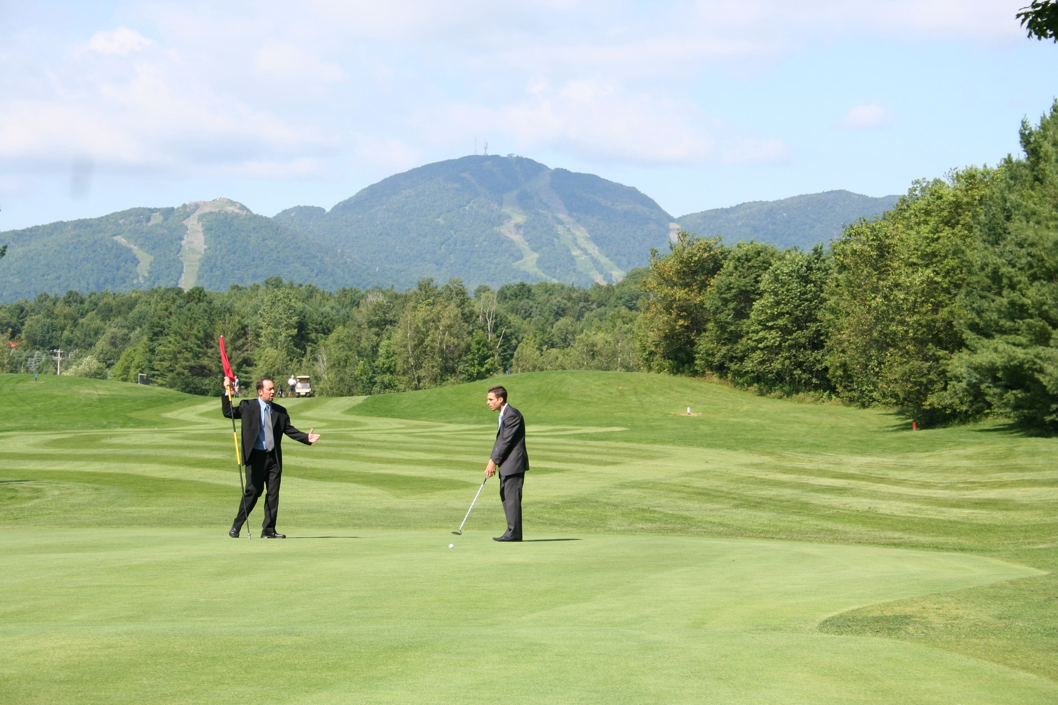 A golf course with two individuals in suits, one holding a golf club and the other gesturing.