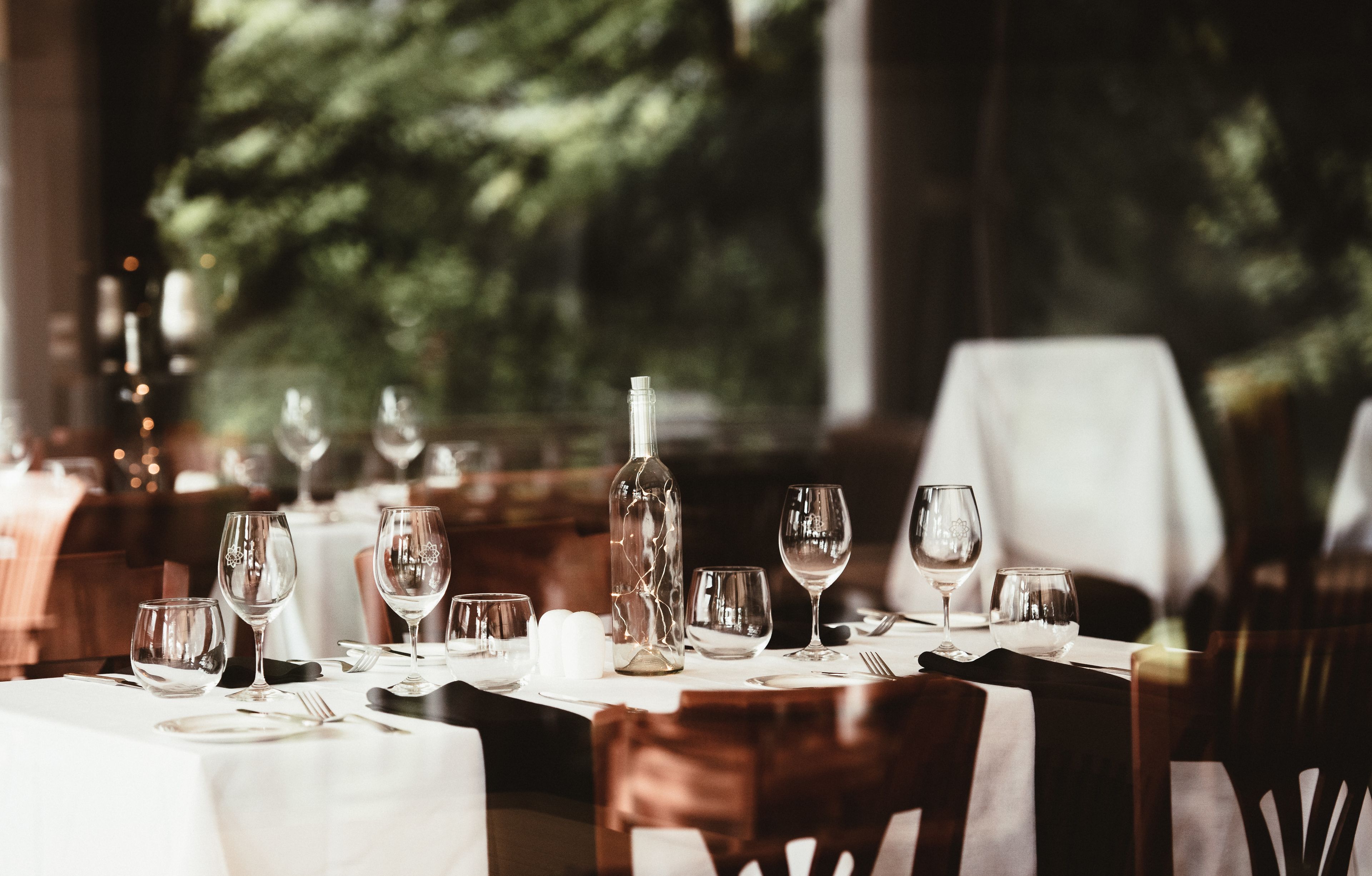 A dining table set with wine glasses, a bottle, and cutlery, with a view of trees in the background.