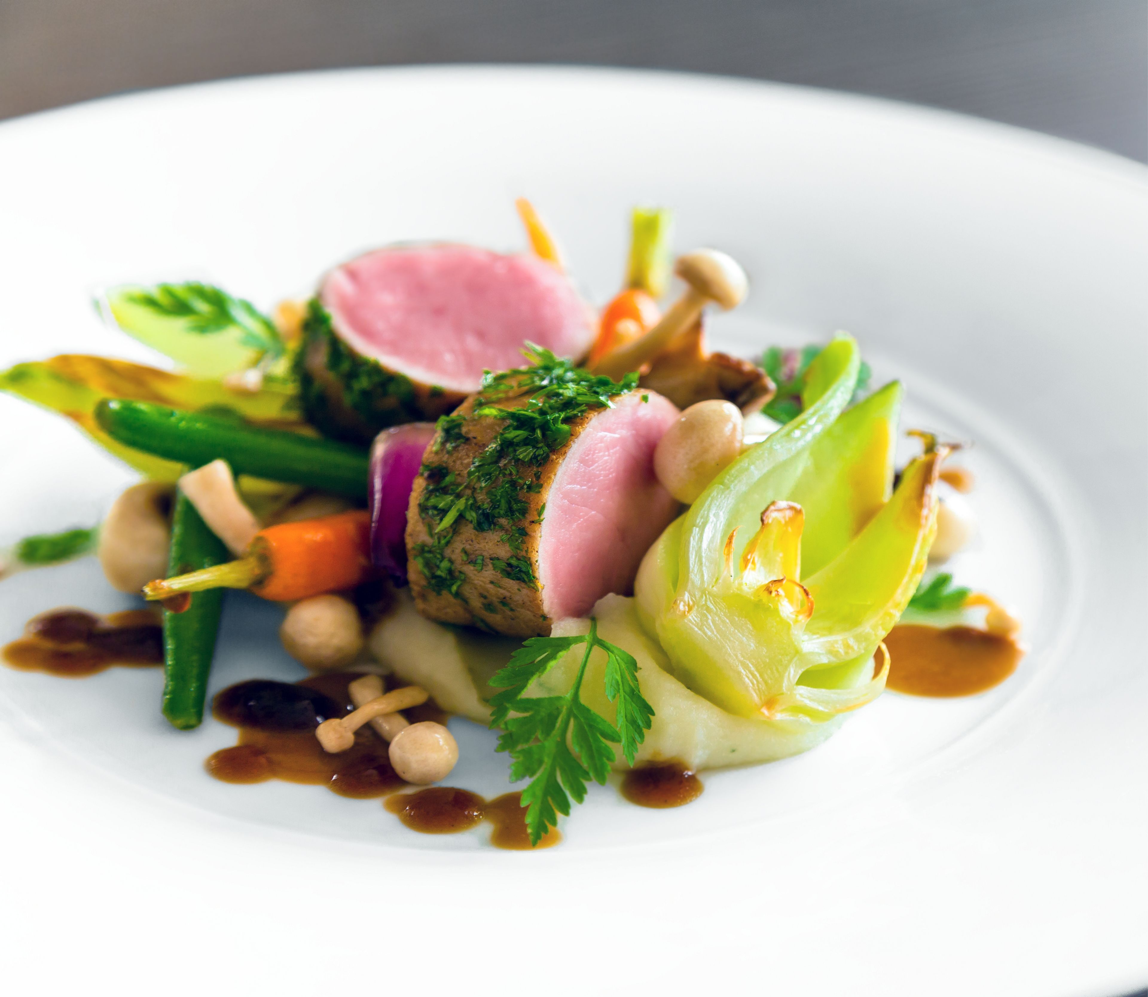 Un plat composé de différentes sortes de légumes et d’une tranche de viande, probablement du porc, le tout agrémenté d’herbes aromatiques.