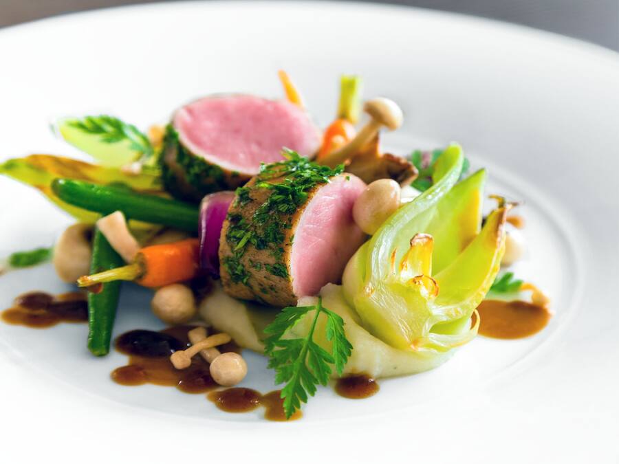 Un plat composé de différentes sortes de légumes et d’une tranche de viande, probablement du porc, le tout agrémenté d’herbes aromatiques.