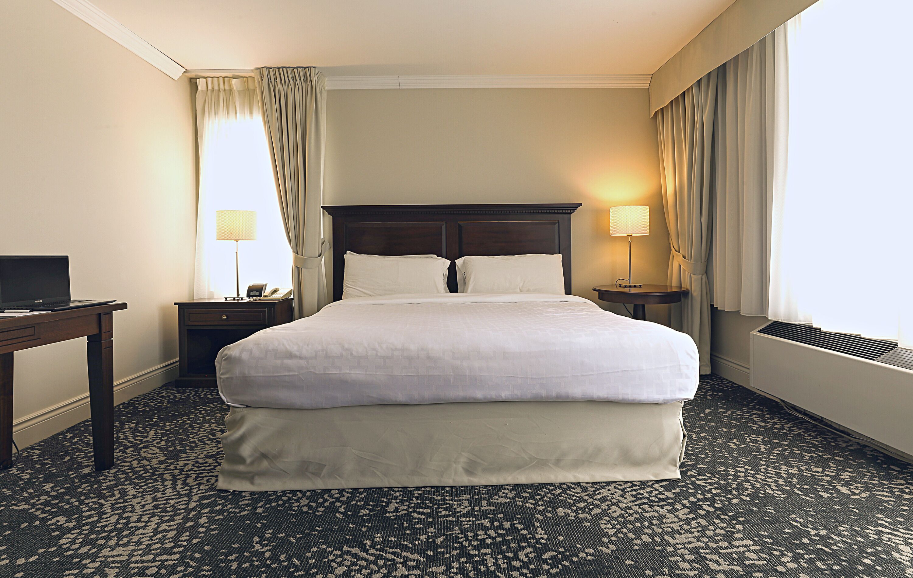 Une chambre d’hôtel avec un grand lit, deux tables de chevet, un bureau et une fenêtre avec des rideaux.