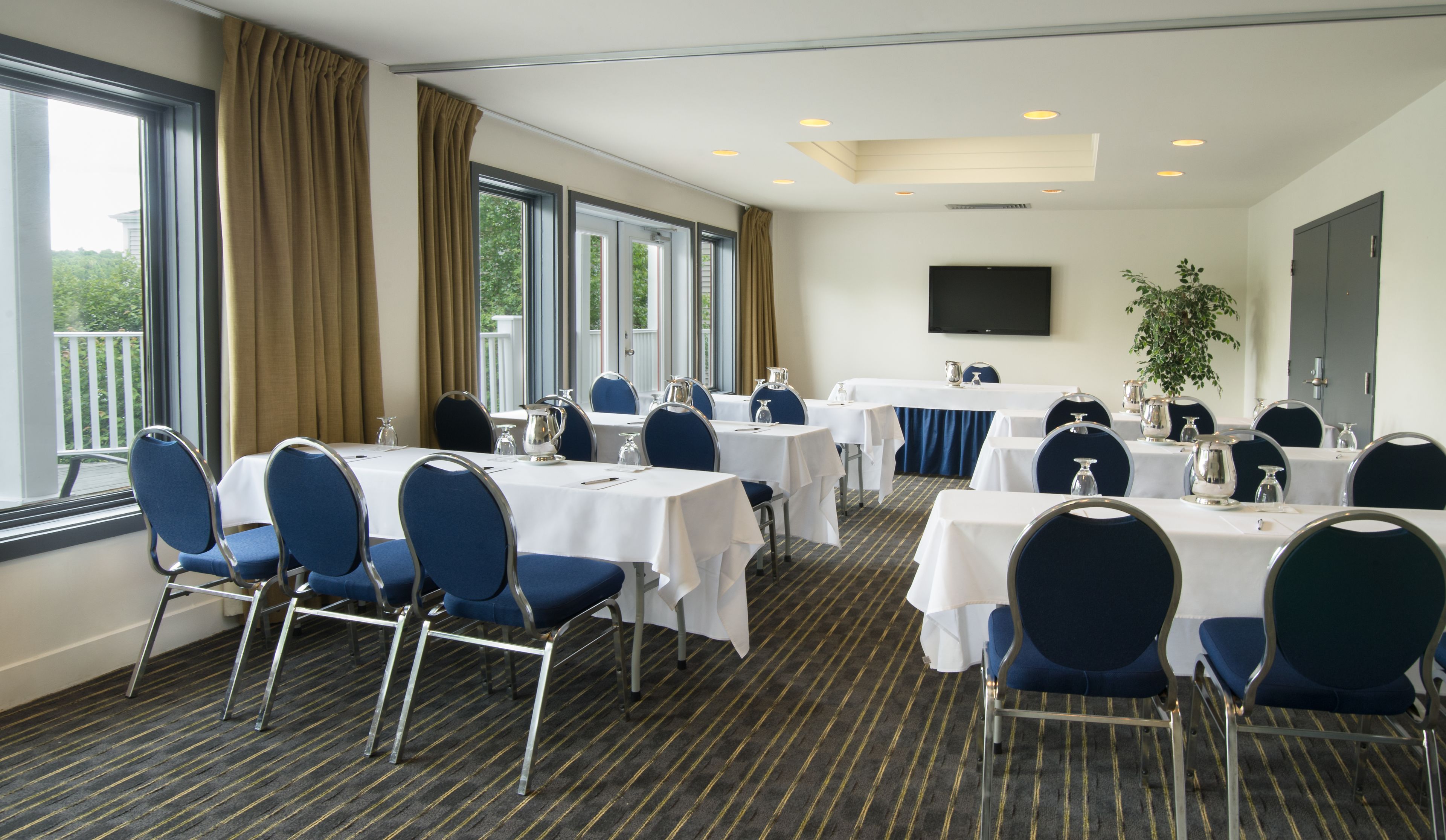 A conference room with tables and chairs, large windows, and a flat-screen TV on the wall.