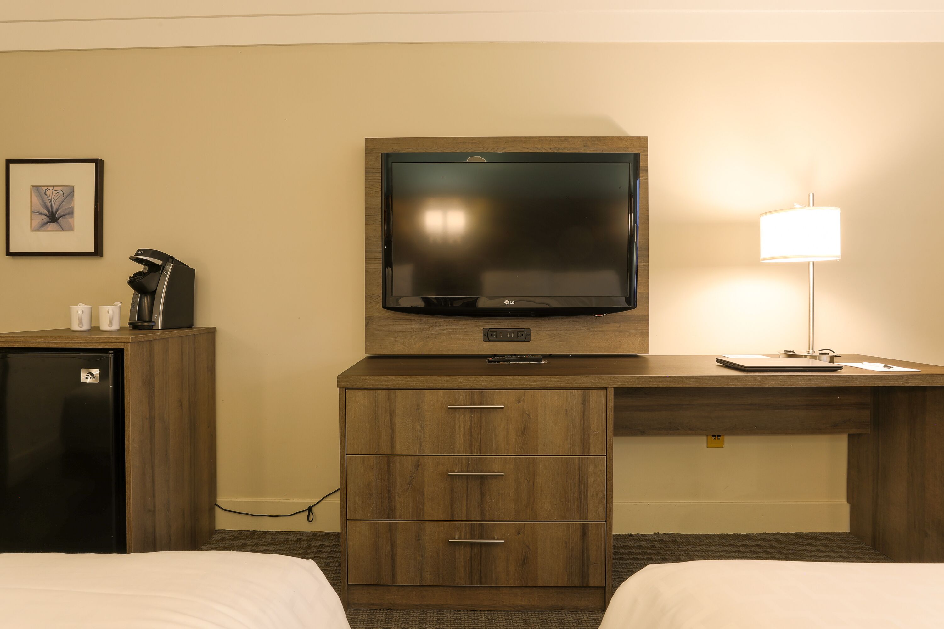 Et hotelværelse med en seng, et skrivebord med TV, en lampe og et minibar.
