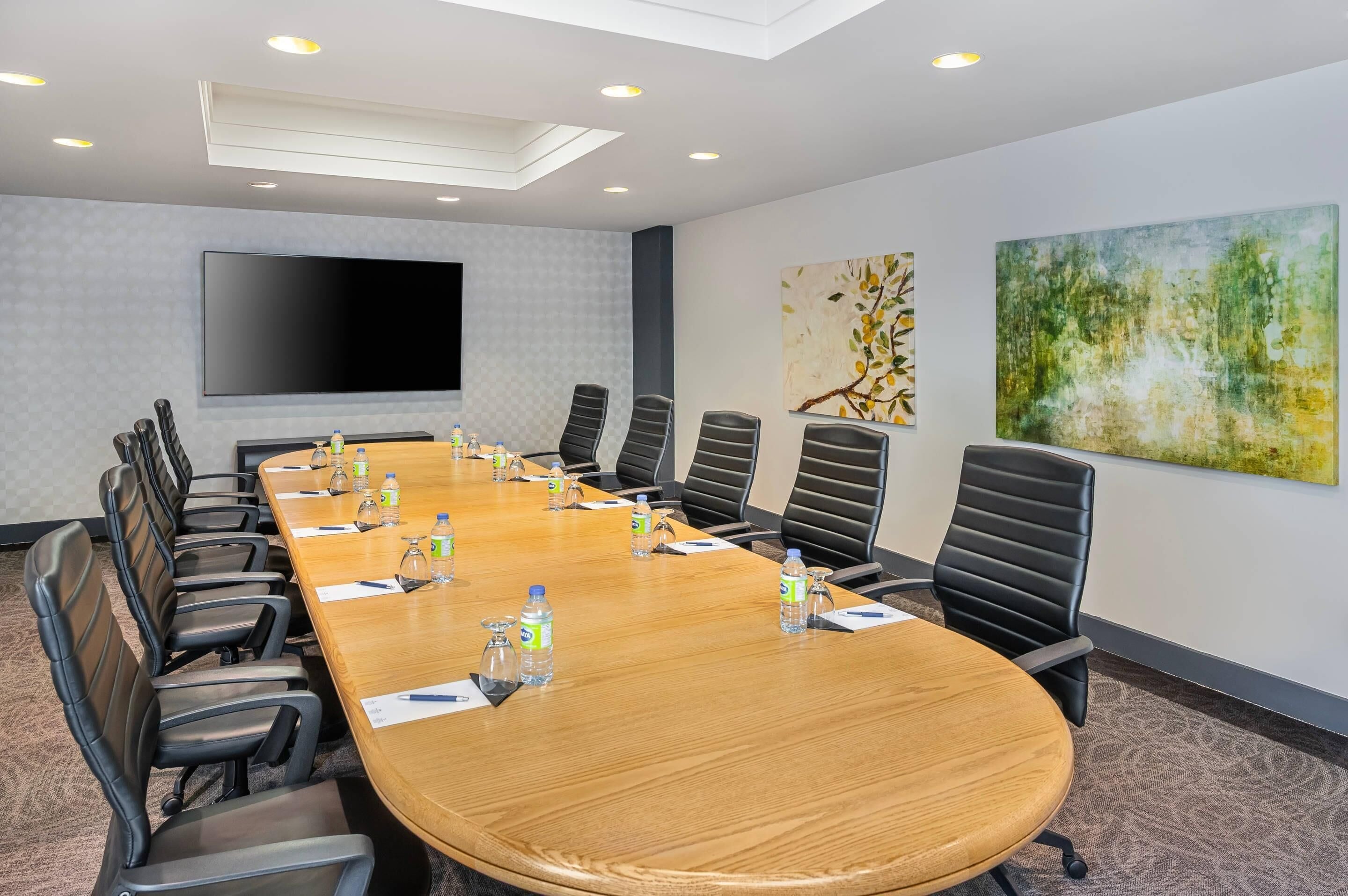 A conference room with a long table, black chairs, water bottles, and a large screen.