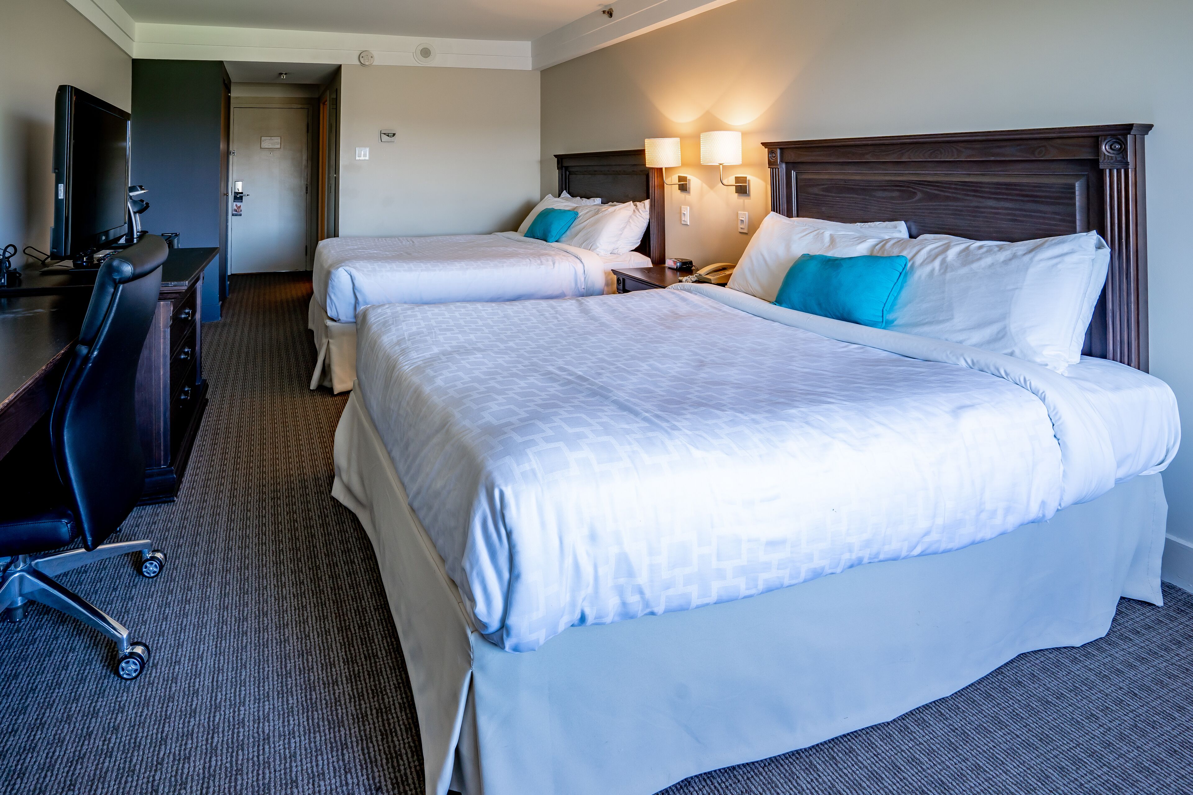 A hotel room with two beds, a desk with a chair, a television, and two wall-mounted lamps.