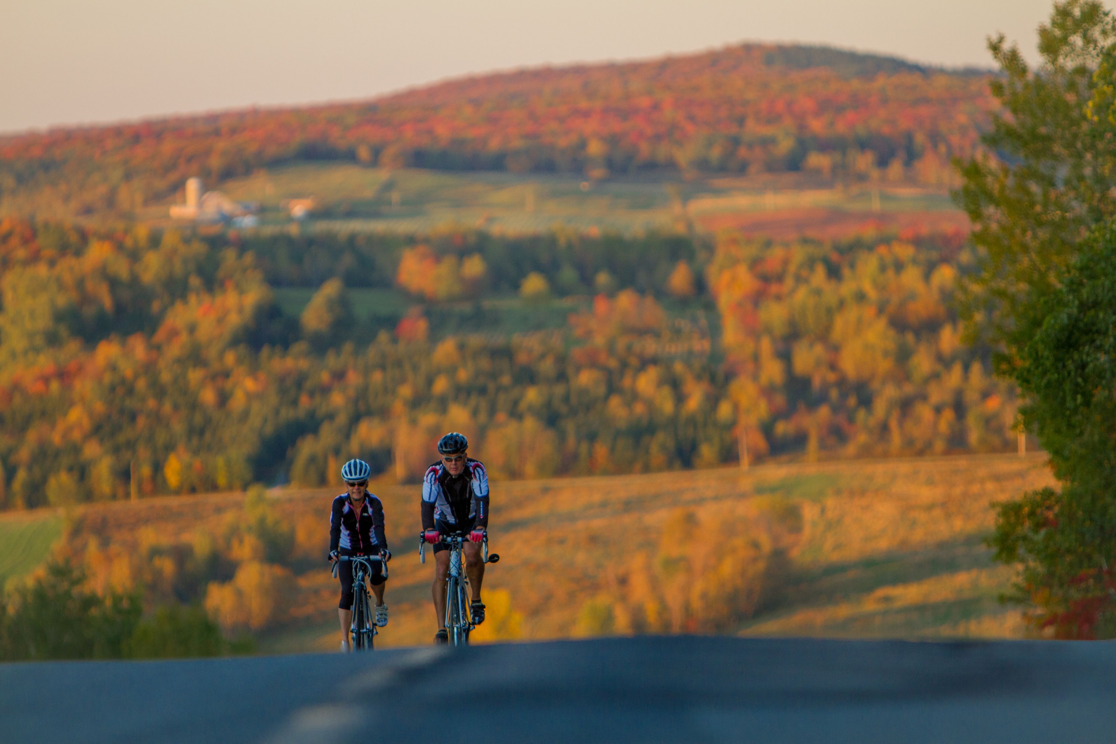 Two cyclists on a road with a hilly landscape in the background.