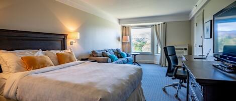 Una habitación de hotel con una cama grande, un sofá, un escritorio con computadora y un televisor.