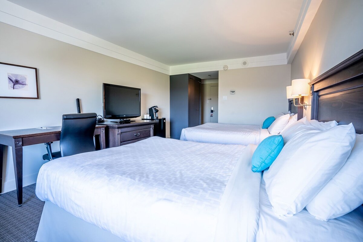 Habitación de hotel con dos camas, un escritorio con computadora, televisión y cafetera.