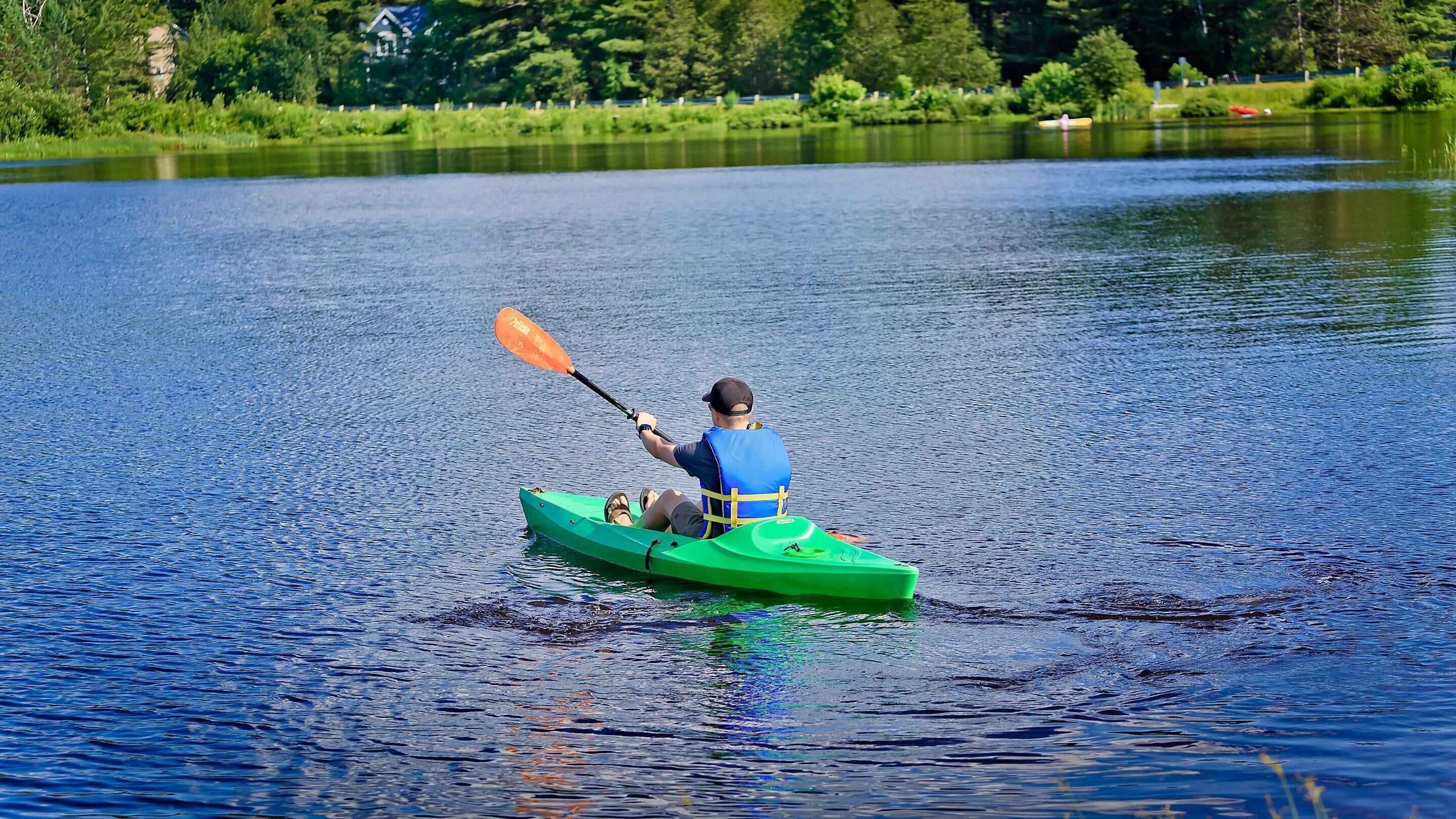 Une personne fait du kayak sur un lac paisible, avec une maison en arrière-plan.