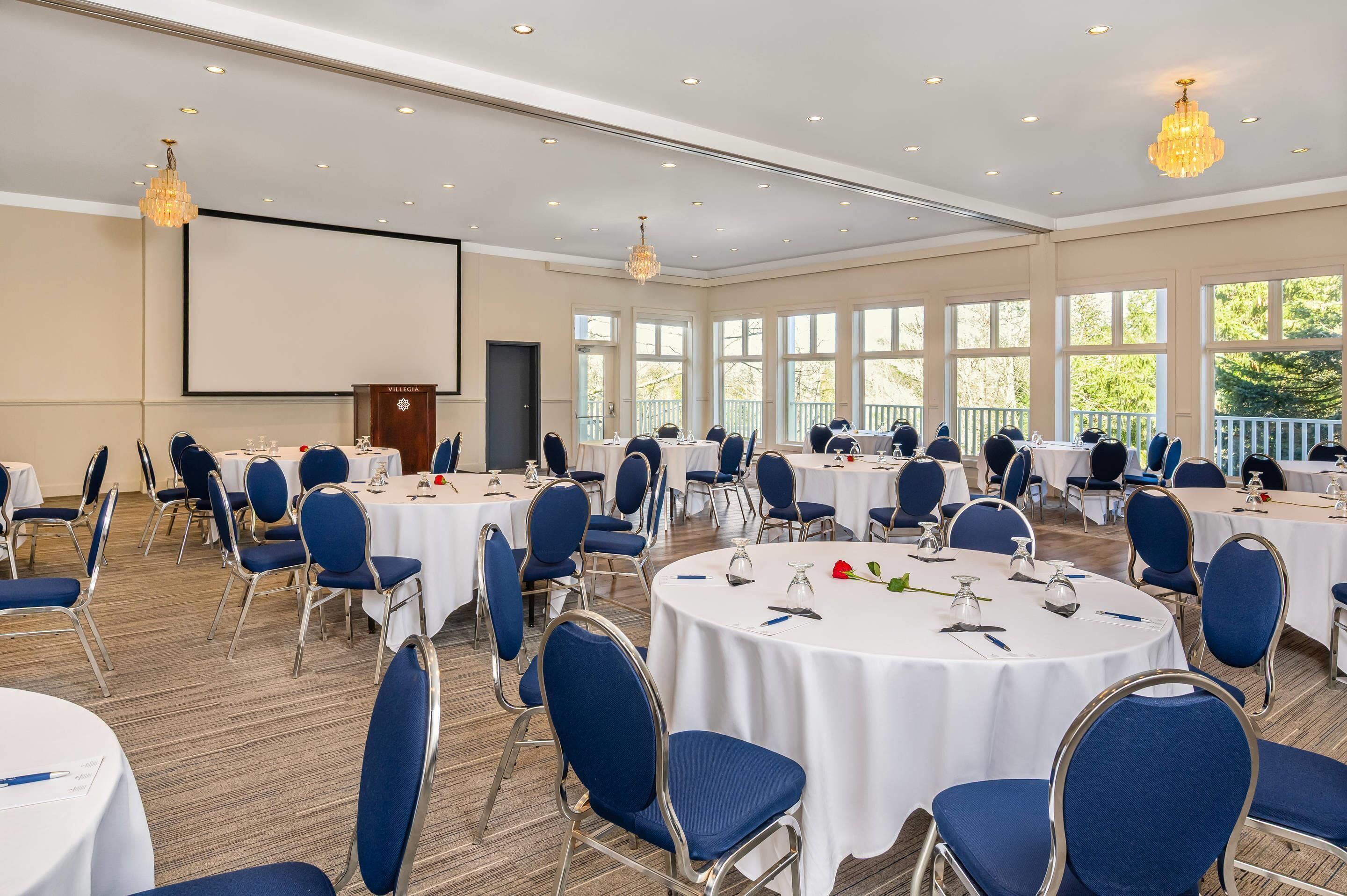 A conference room with round tables, blue chairs, and a projector screen.