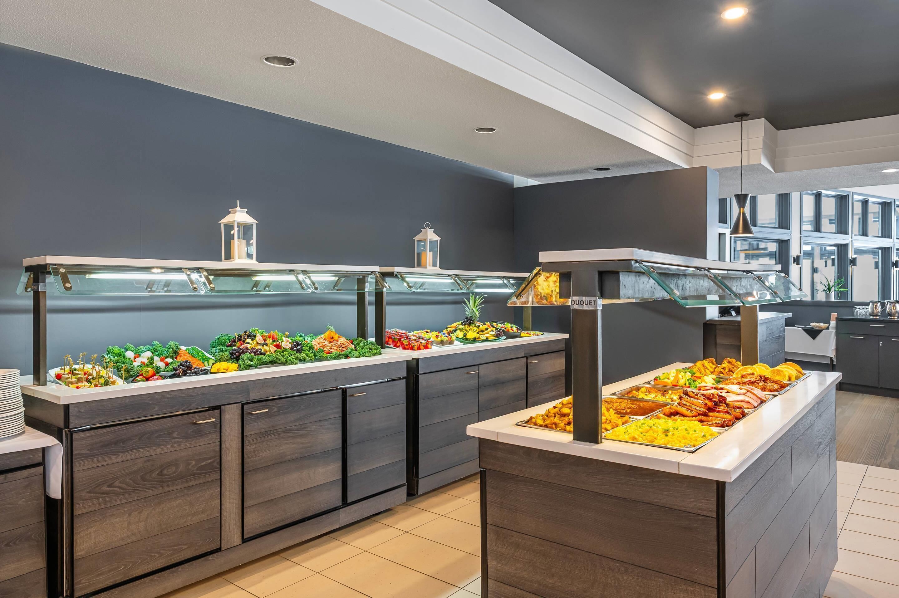 A buffet area with multiple food stations, including a duquet section, in a modern hotel setting.
