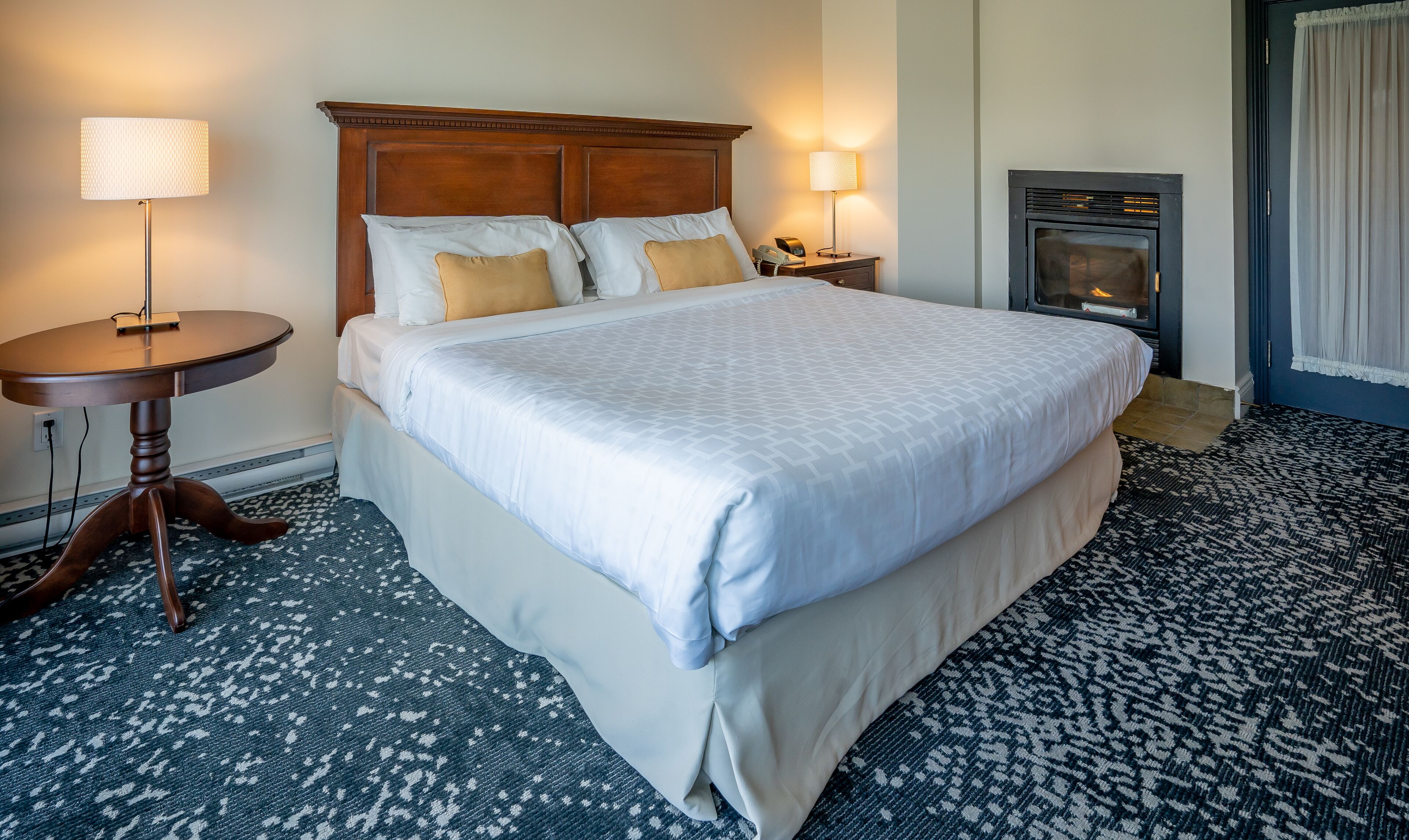 Une chambre d’hôtel avec un grand lit, une table de chevet, une lampe, un téléphone et une cheminée.