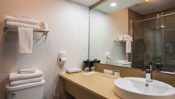 A modern bathroom with a toilet, sink, and large mirror. There are towels on a shelf and a hairdryer on the wall.