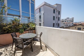 A balcony with a round table and four wicker chairs, overlooking a cityscape with modern buildings. - Cannes Croisette Prestige (Cannes)