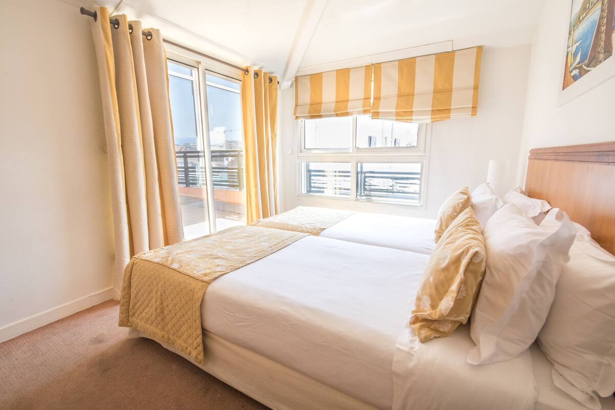 Una cama doble con una colcha acolchada, una ventana con vistas y una cortina.