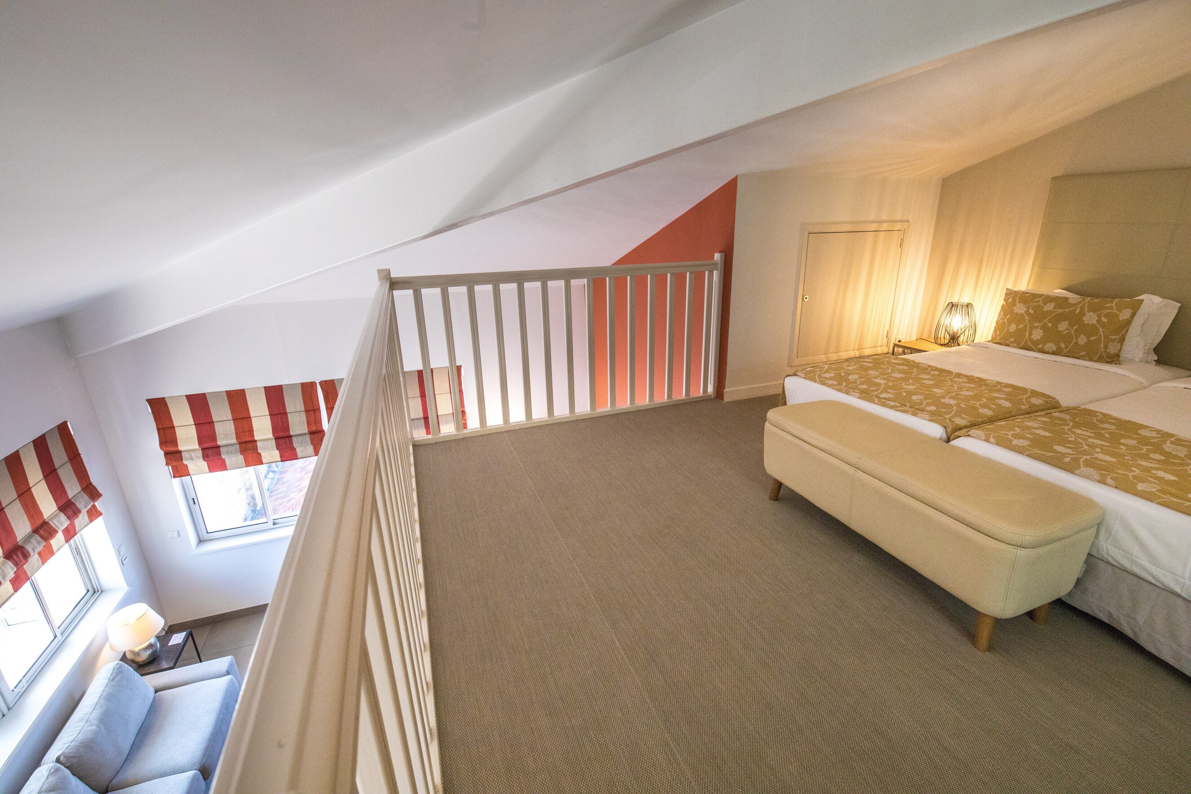A bedroom with a large bed, a bench, a window with curtains, and a view of the outside.