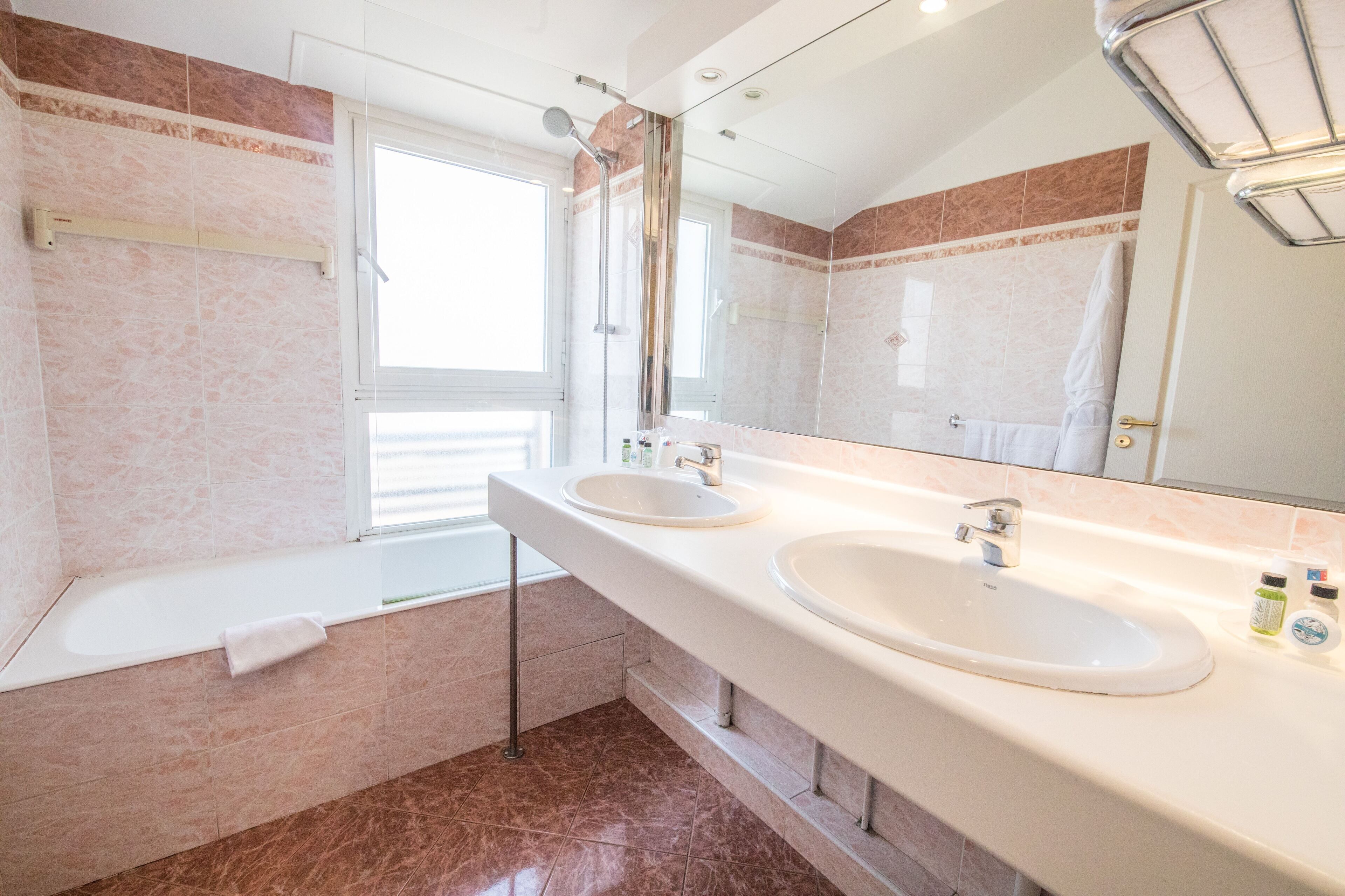 A modern bathroom with two sinks, a bathtub, and a large mirror.