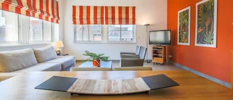 Una sala de estar con un sofá, una mesa de centro, un televisor y obras de arte en la pared.