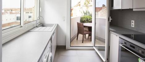 Una cocina funcional con lavadora, un comedor con mesa y sillas, y vista al vecindario a través de un ventanal corredera.