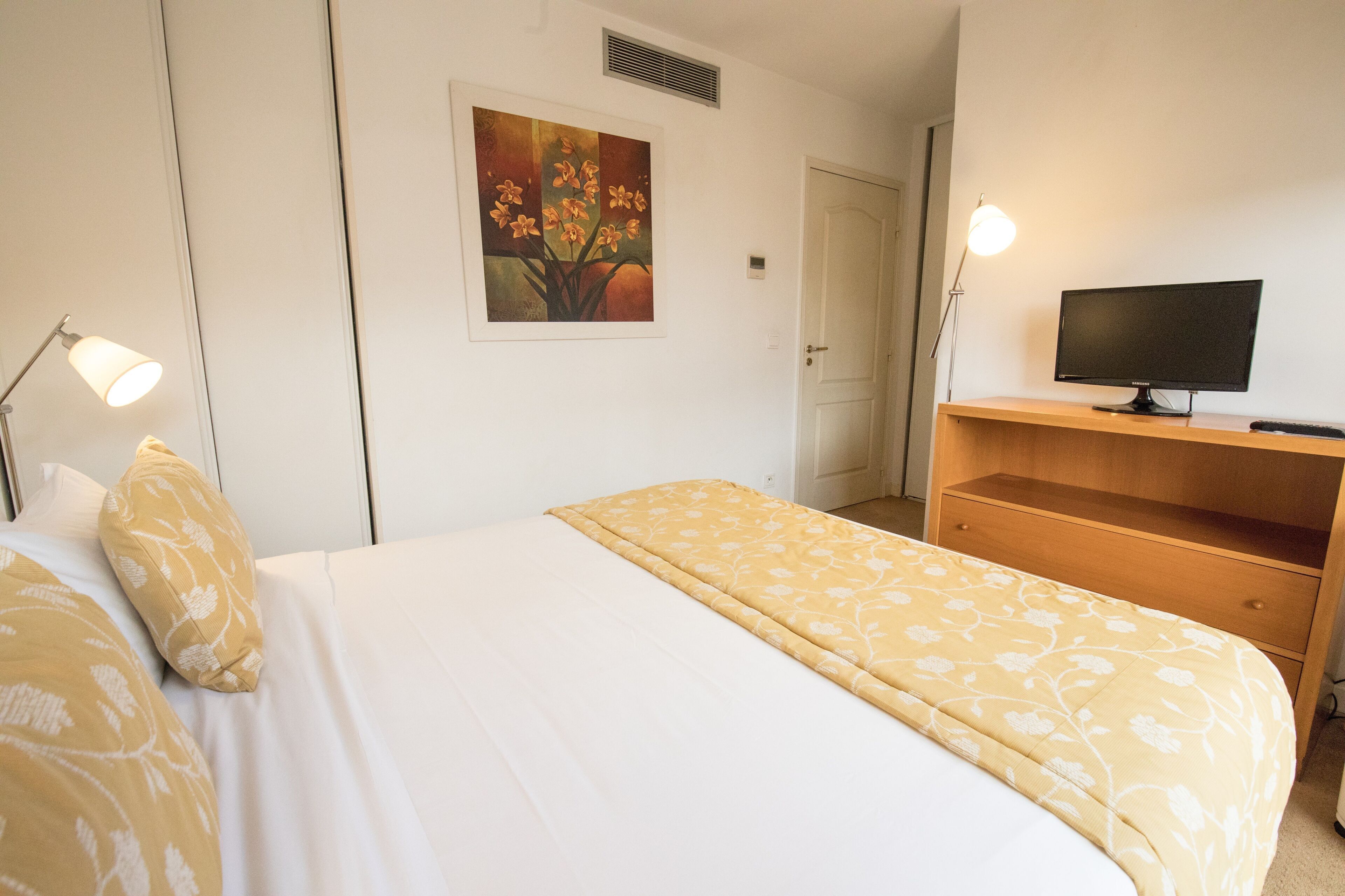 Ein Hotelzimmer mit Bett, Schreibtisch mit Computer, einem Bild an der Wand und einer Tür.