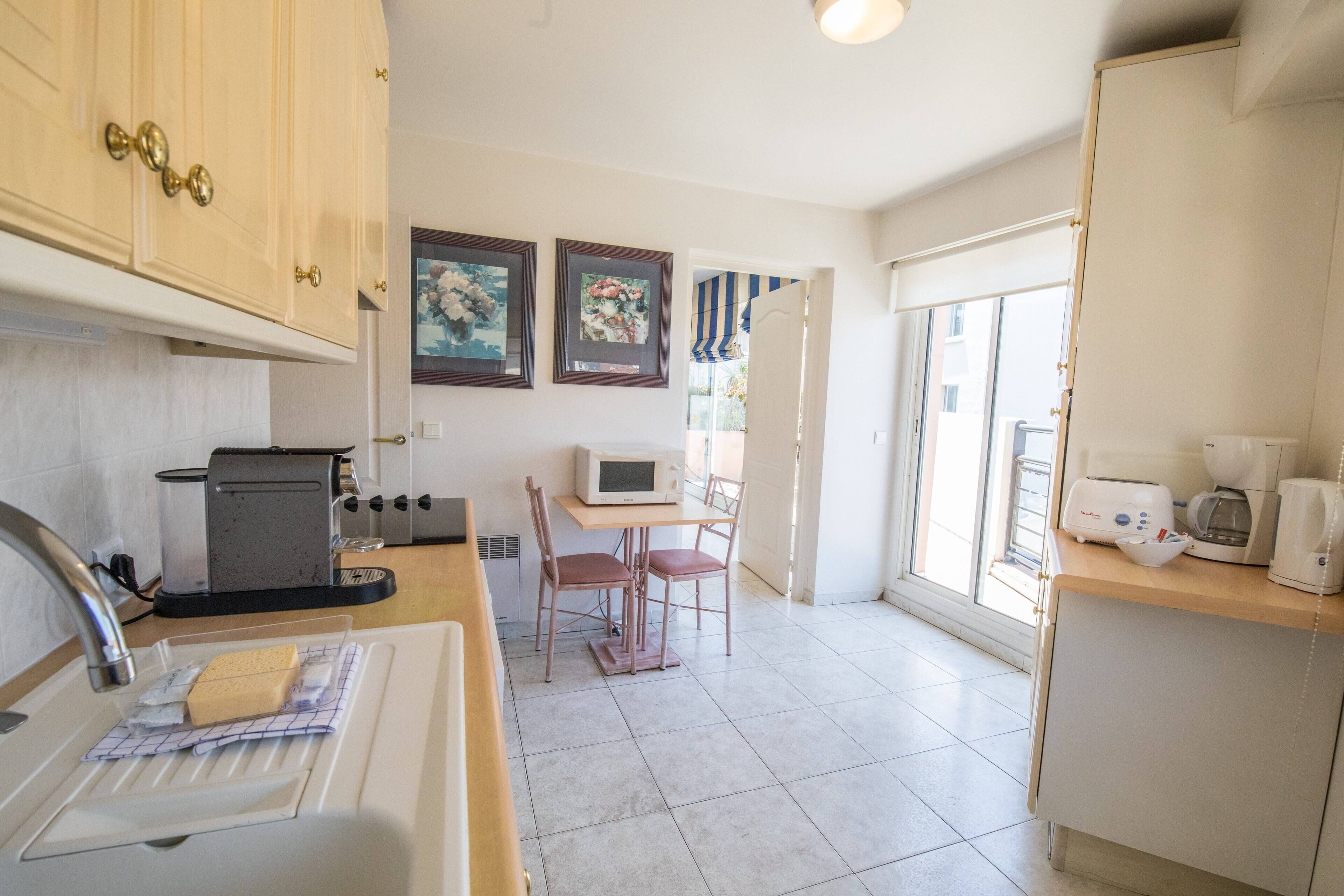 A kitchen with a sink, a microwave, a toaster, and a coffee maker. There is a table with chairs and a window with a view of the outside.