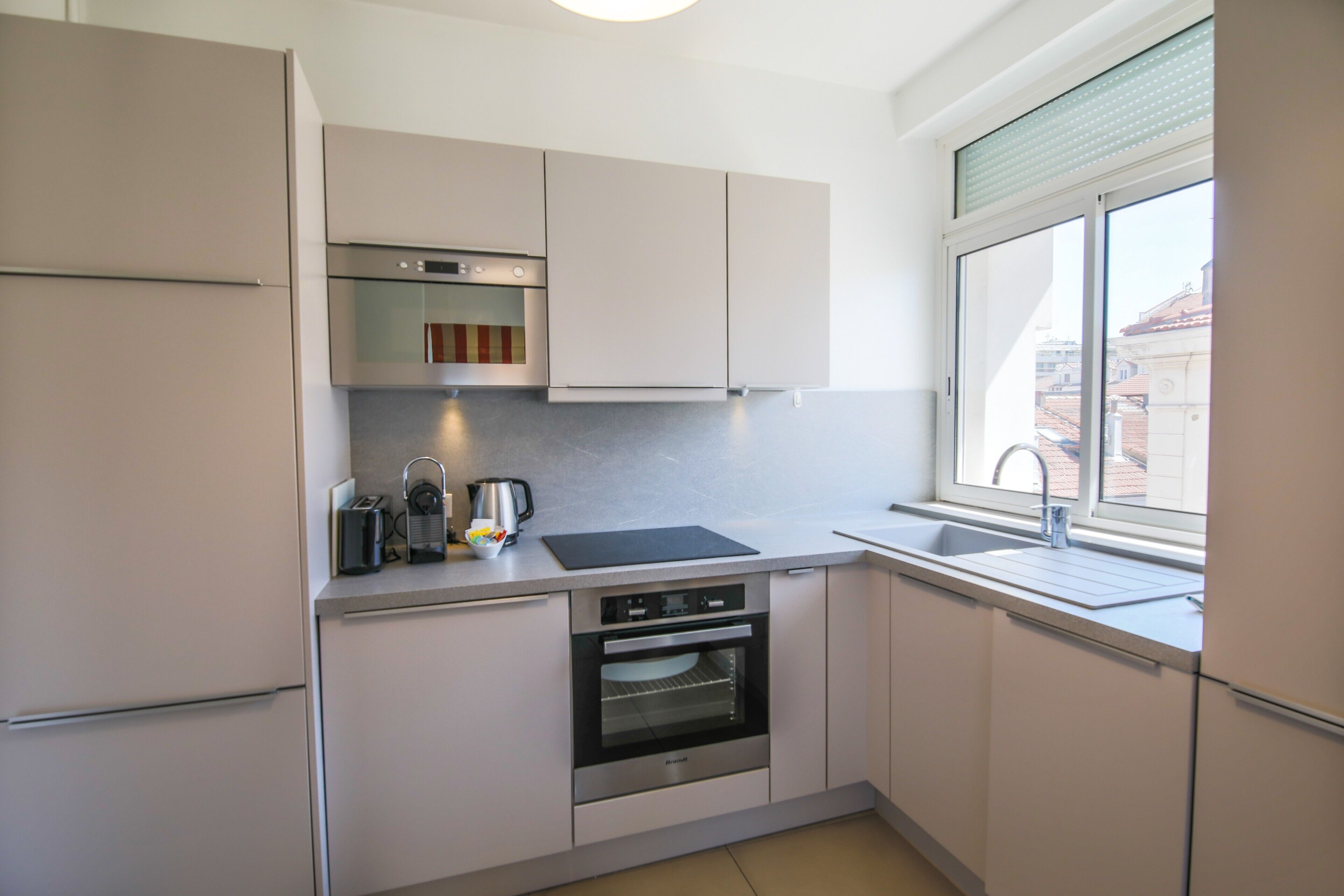 A modern kitchen with a built-in oven, a sink, and a window providing a view of the outside.