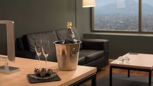 Quarto com vista para a cidade e montanhas, mesa com garrafa de champanhe, copos e morangos, e um abajur.