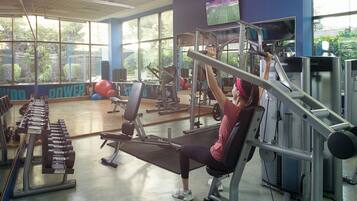 A gym with various exercise equipment, large windows, and a television screen.