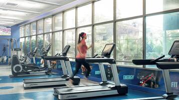 A gym with treadmills, weight machines, and a large window with a view of greenery.