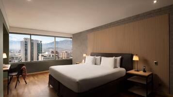 Una habitación de hotel moderna con una cama grande, un escritorio y una silla. La habitación ofrece vistas a la ciudad a través de amplios ventanales.