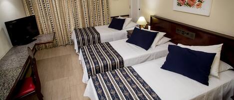 Habitación de hotel con dos camas, un escritorio con silla, un televisor y un cuadro en la pared.