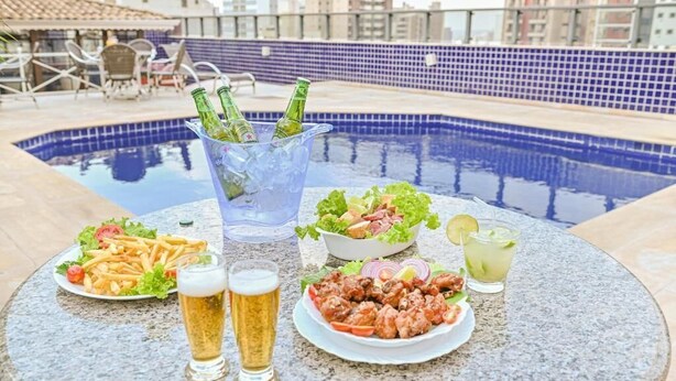 Mobiliario de comedor junto a la piscina, con una mesa, platos de comida, bebidas y una piscina al fondo.