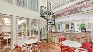 Un restaurante con una escalera de caracol, sillas rojas con estampado floral y una zona de bar.