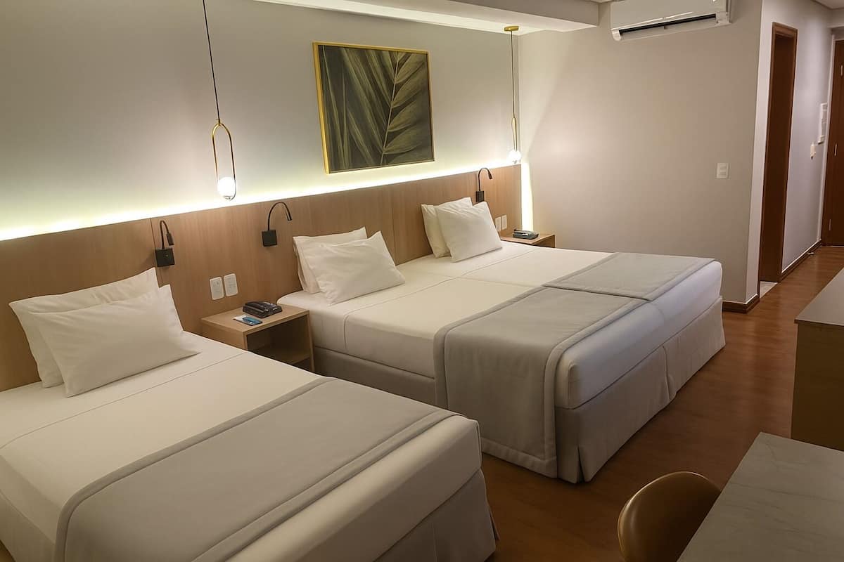Una habitación de hotel con dos camas, una mesita de noche con lámpara, una obra de arte en la pared y suelo de madera.