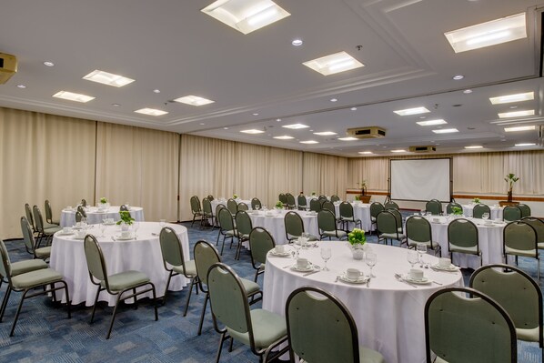 Un salón de conferencias con varias mesas redondas, cada una dispuesta con sillas, platos y vasos.