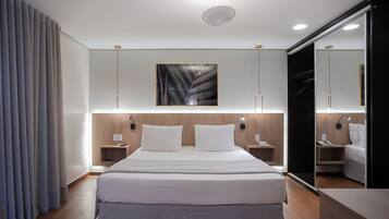 A modern hotel room with a large bed, bedside tables, a mirror, and a wall-mounted artwork.