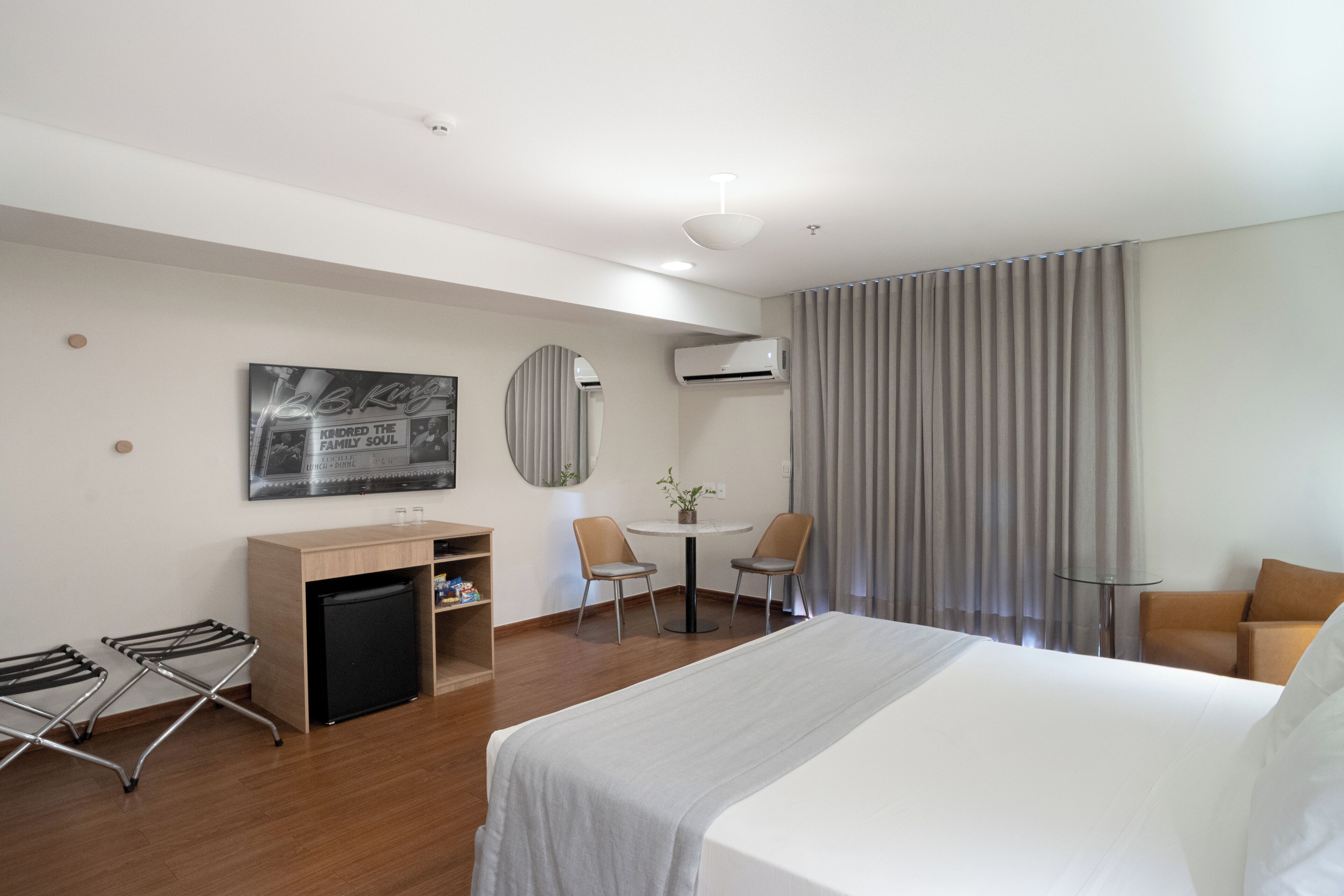 A modern hotel room with a large bed, a desk, a chair, a small table with a plant, and a seating area with a couch.