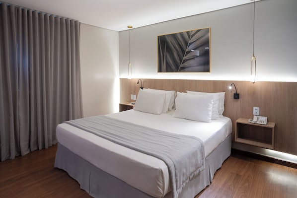 A modern hotel room with a large bed, wooden headboard, bedside tables with lamps, and a wall-mounted artwork.