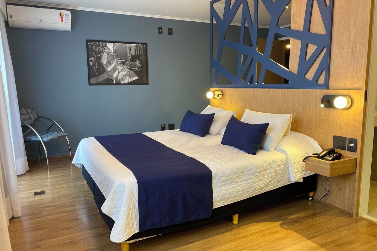 Een net opgemaakt bed met een blauw-witte sprei, een houten hoofdbord en bedlampen.