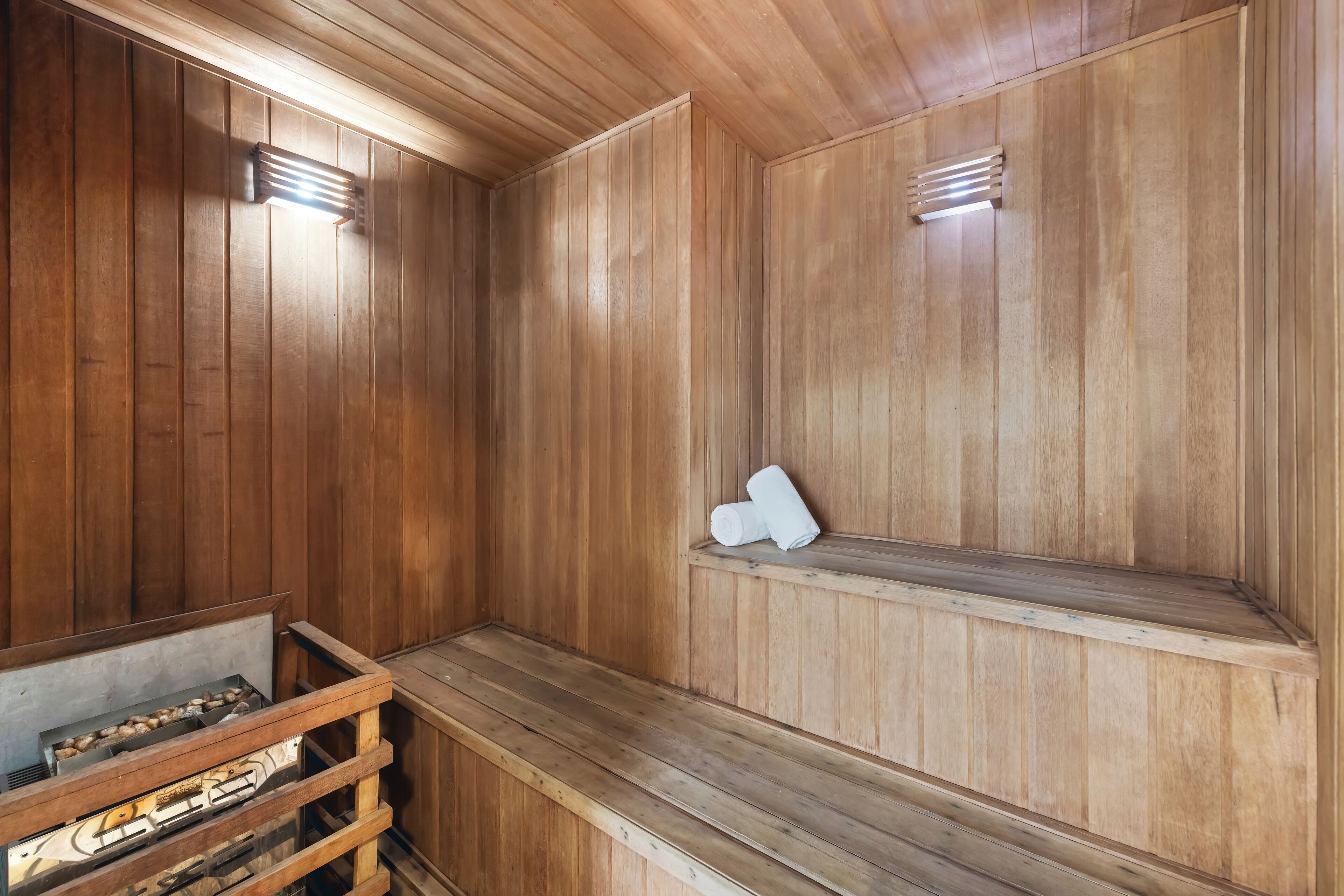 Una sauna con paredes y bancos de madera, un banco con toallas, y un banco de madera con una toalla encima.
