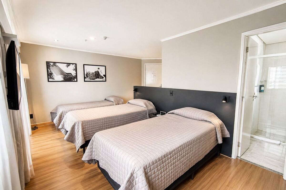 Een hotelkamer met drie bedden, een douche en een muur met twee zwart-witfoto’s.