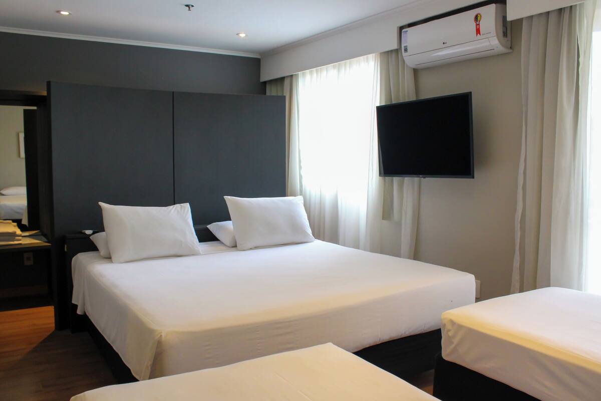 Hotelkamer met twee bedden, een flatscreen-tv, een airconditioning en een nachtkastje met een lamp.