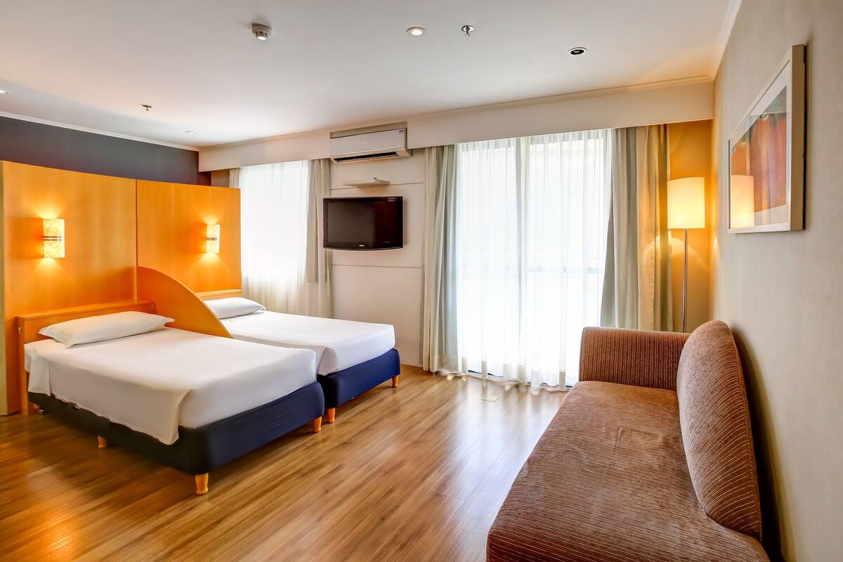 Een hotelkamer met twee bedden, een bank, een televisie en een raam met gordijnen.