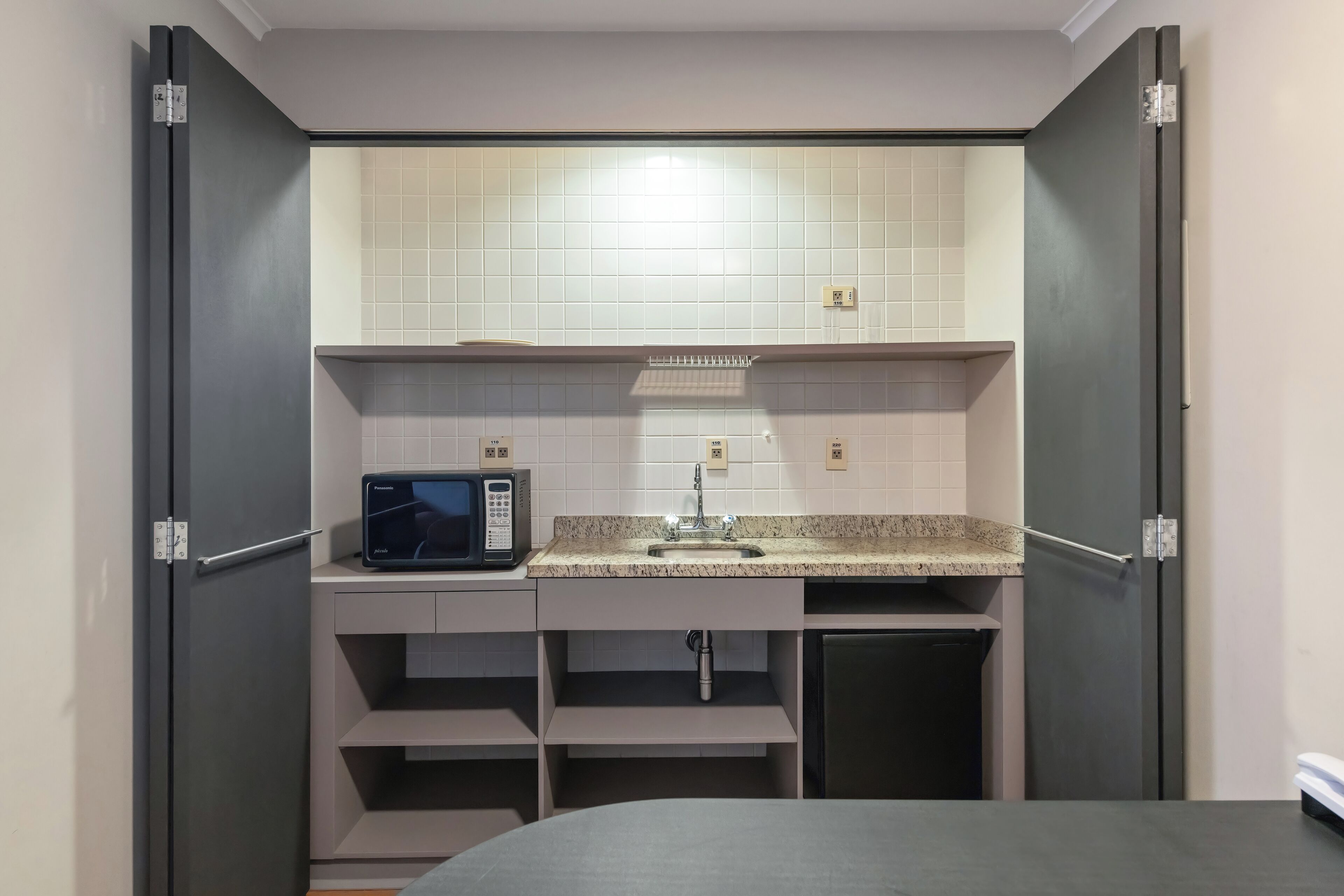 Cocina compacta con microondas, lavamanos y armarios.