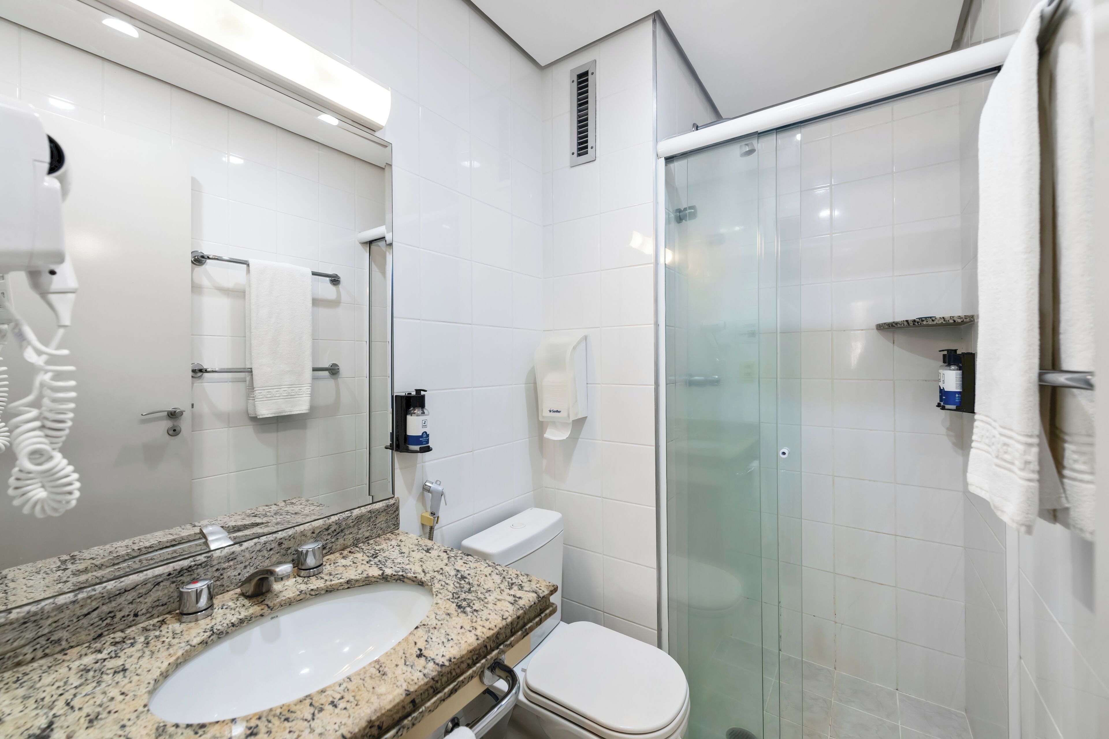 A modern bathroom with a granite sink, white toilet, and glass shower enclosure.