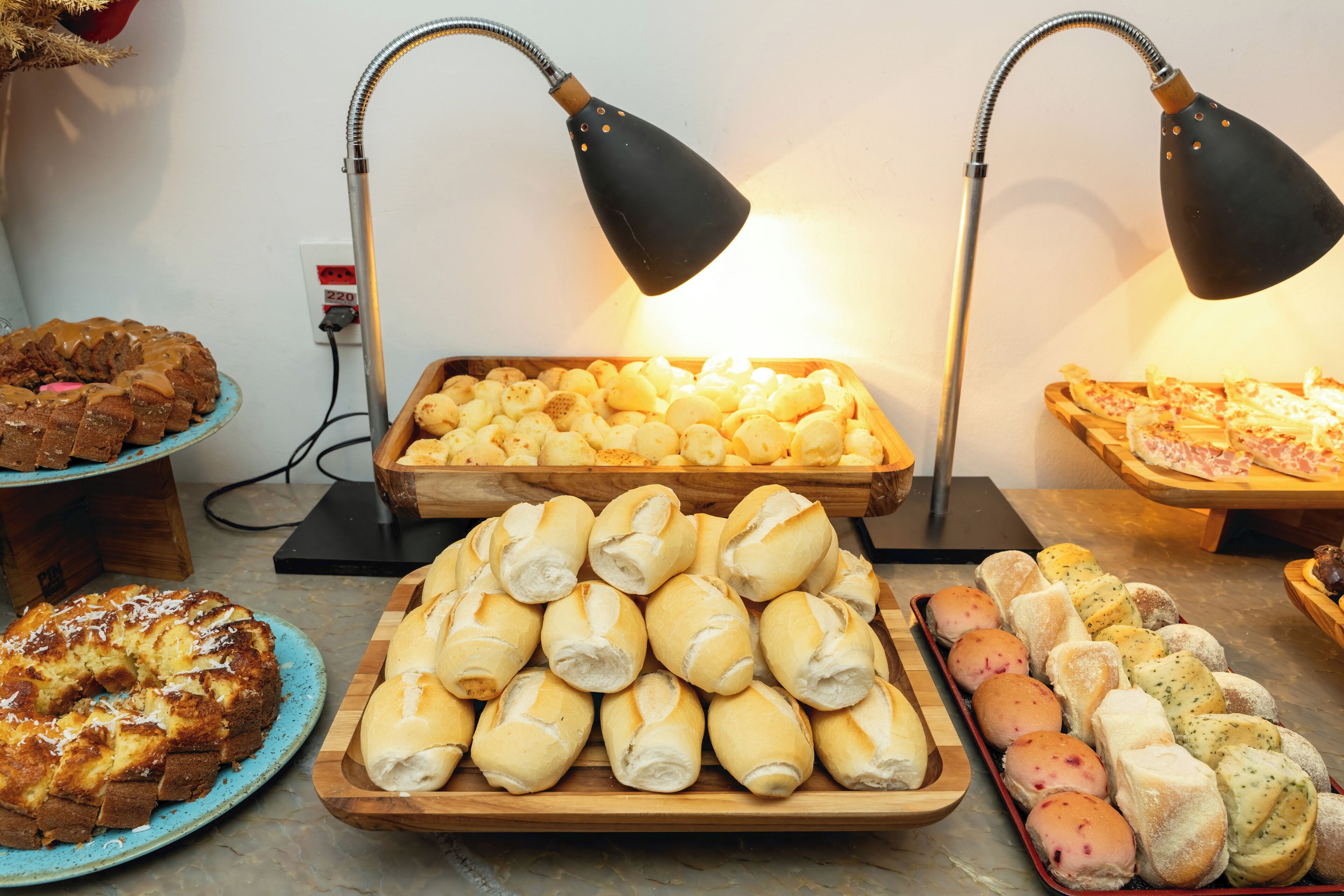 A variety of baked goods displayed on wooden trays, with two black desk lamps illuminating the scene.